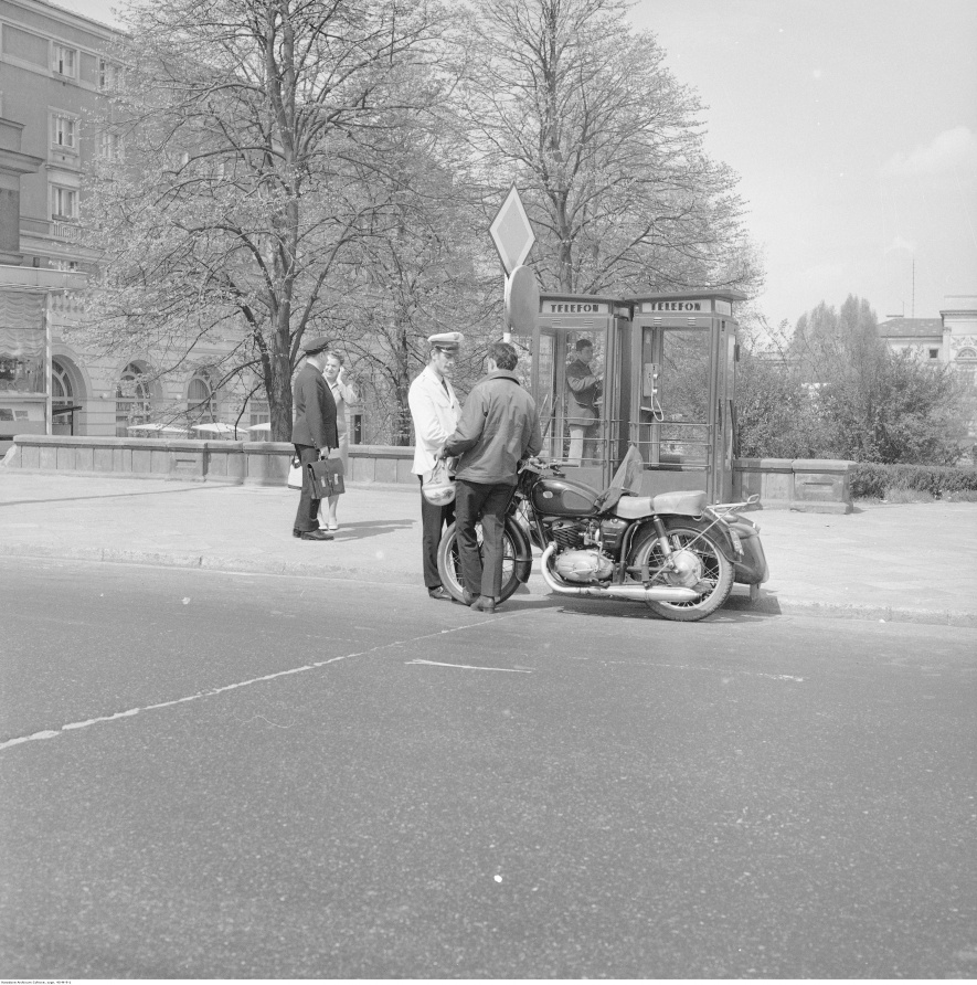 Milicjant kontrolujący motocyklistę przy placu Dzierżyńskiego (obecnie plac Bankowy), 1967-1970, fot. Grażyna Rutowska, Narodowe Archiwum Cyfrowe: 40-M-9-1